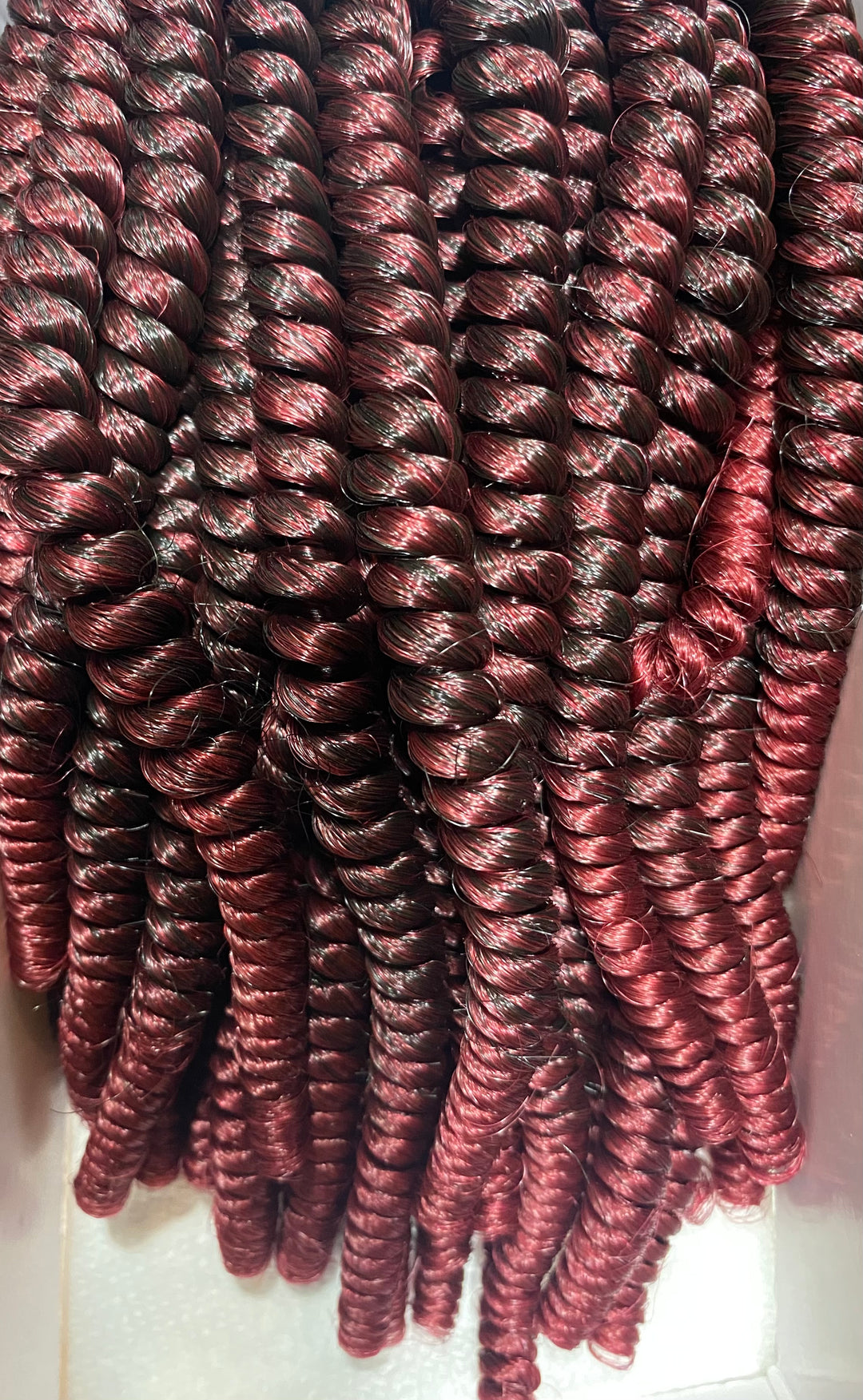 A bunch of Kadi Natural Spring Twist burgundy colored curls in a Kadi Naturals box, promoting natural hair care and skincare.